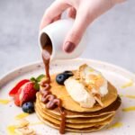 a-woman-s-hand-pours-caramel-on-a-stack-of-pancake-2024-10-18-03-55-25-utc